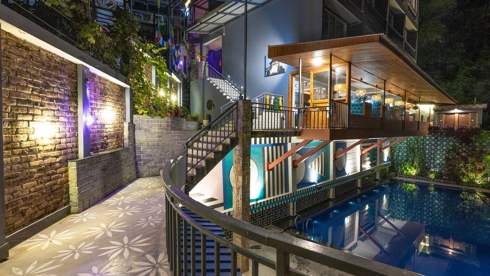 An image of a entrance which has a swimming pool on one side and the entrance leads to a well lit building - Avianna Group of Hotels & Resorts