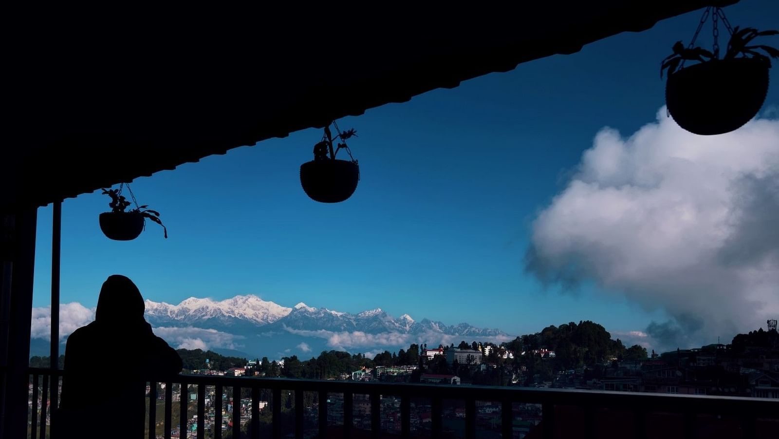 Image of a women standing in the balcony overlooking the clear sky and mountain valley.