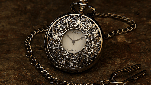Antique silver pocket watch with intricate design placed on a rustic surface.