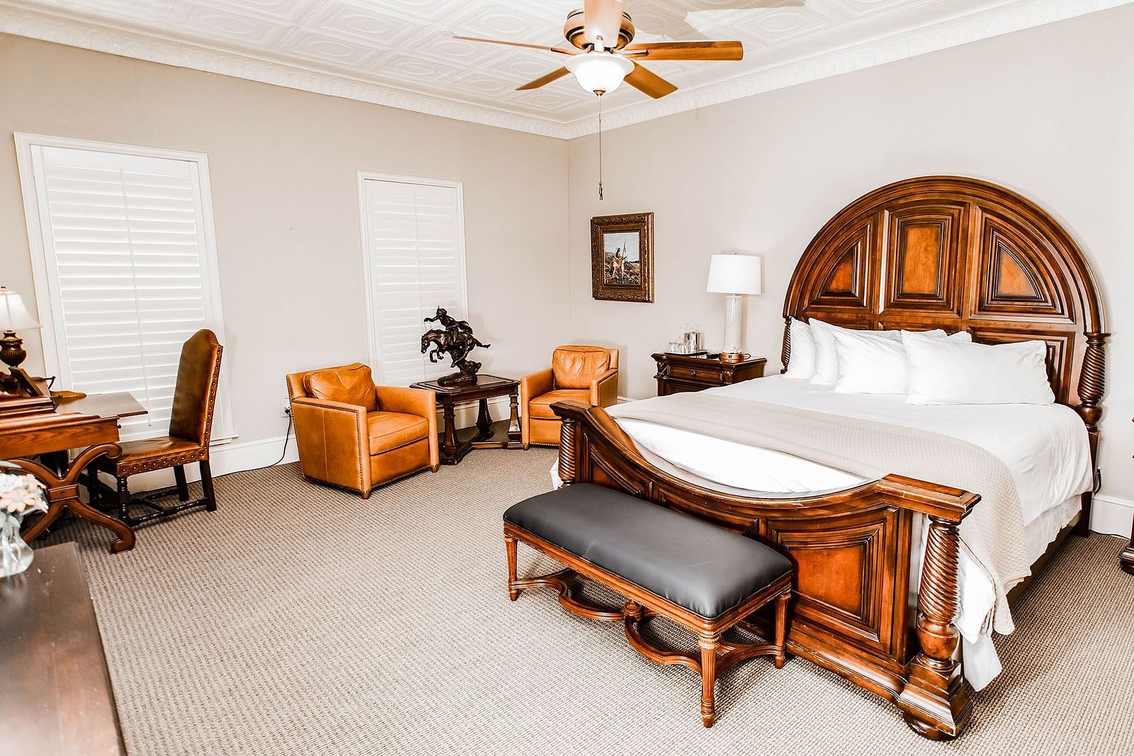 A traditional bedroom featuring a wooden bed, elegant decor, and a ceiling fan, providing a comfortable and timeless space - The Grand Hotel & Ballroom, McKinney
