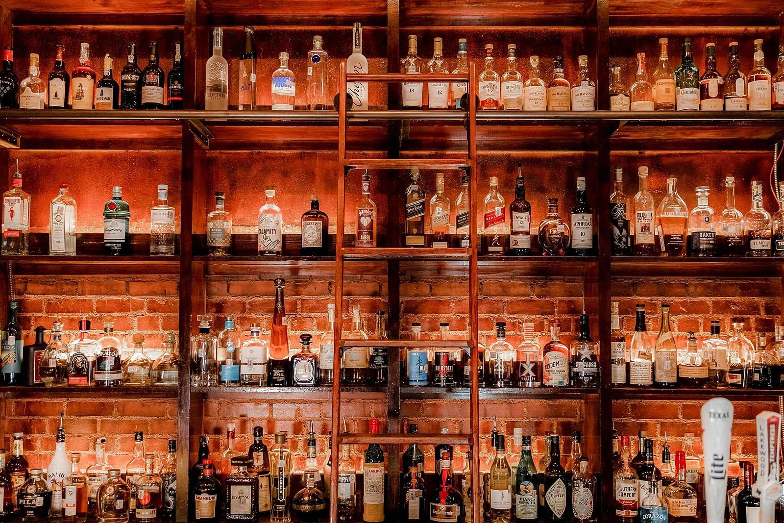  A bar filled with numerous liquor bottles, neatly arranged on shelves, creating an inviting atmosphere for drinks and socialising - The Grand Hotel & Ballroom, McKinney