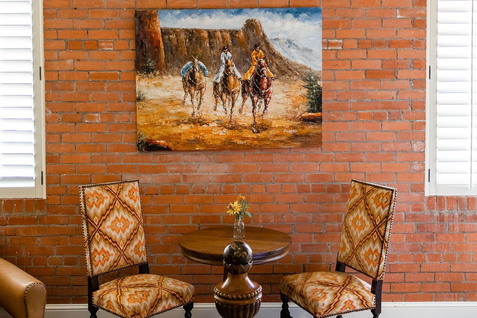 A room with a rustic brick wall, a beautiful painting of horses, and stylish seating, creating a warm, artistic atmosphere - The Grand Hotel & Ballroom, McKinney