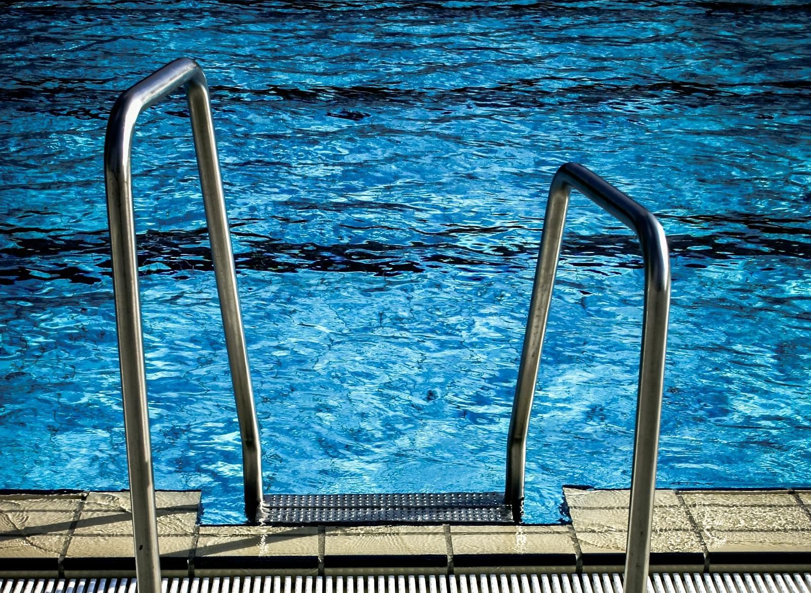 Two metal handrails lead into a swimming pool with blue water.