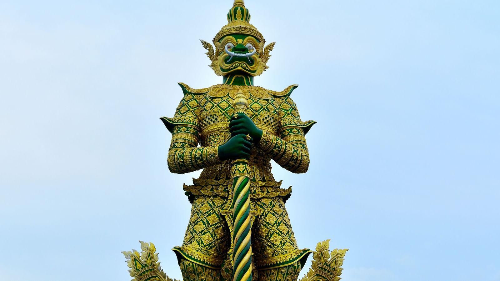 A giant bronze statue near Phra Mondop with blue sky in the background.