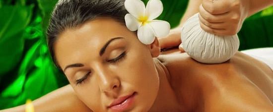 Woman receiving a herbal poultice massage on her shoulder in a spa setting.