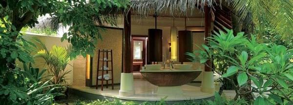 A small cottage with 2 wash basins, and a towel rack, surrounded by green plants and trees at Hotel Mamallaa Heritage, Mahabalipuram.