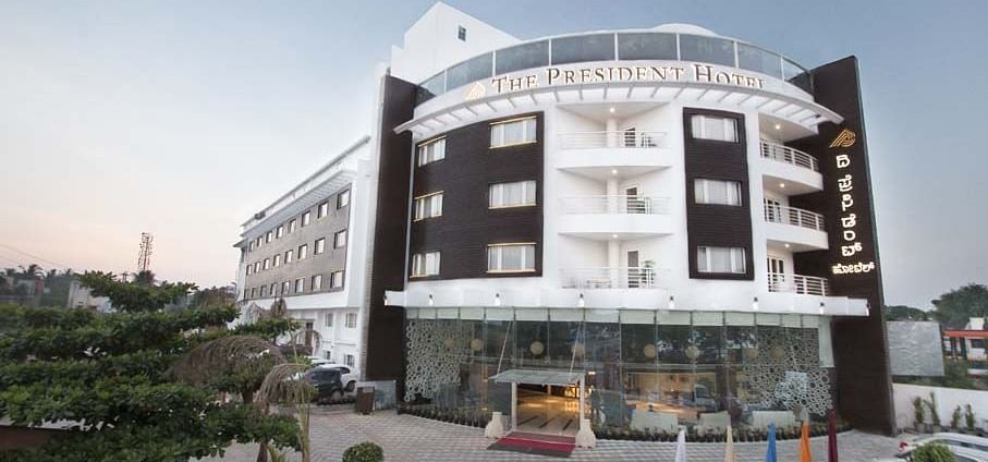 A facade image  with a huge parking area where cars are also parked - The President Hotel,Hubli