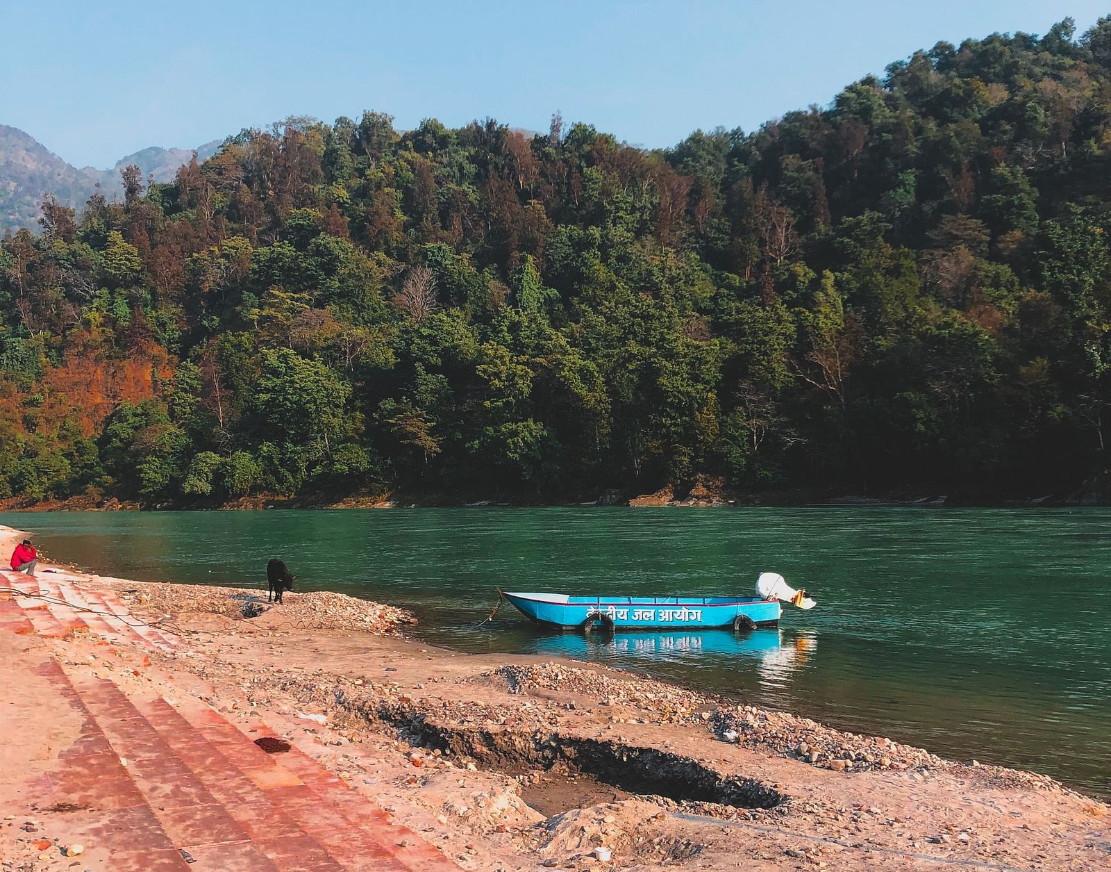 a solitary boat parked on the beach with forest cover in the background