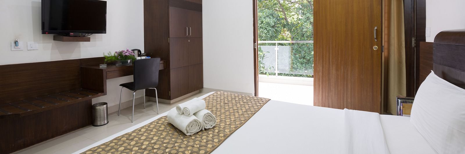 A room with a double bed, a work desk and a chair, wardrobe, and an open door to the balcony - Sanctum Suites BEL Road, Bangalore
