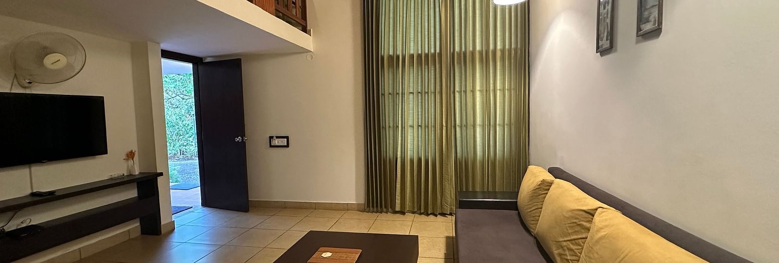 a living room with a long sofa and a television on the wall - Kadkani River Resort, Coorg