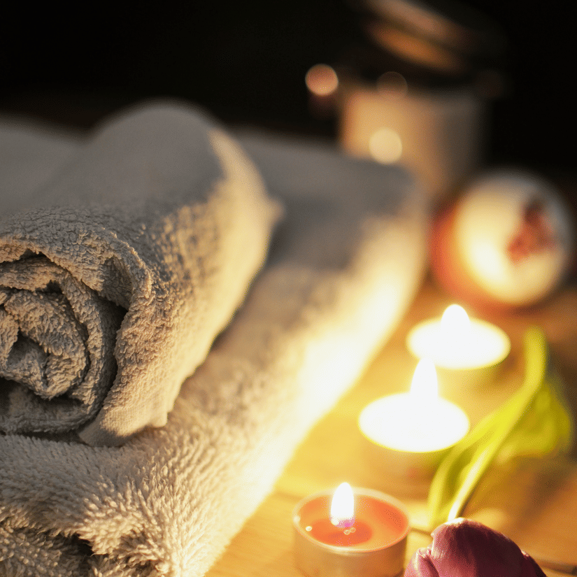 A close up shot of a table with towels and lit tea light candles next to it.