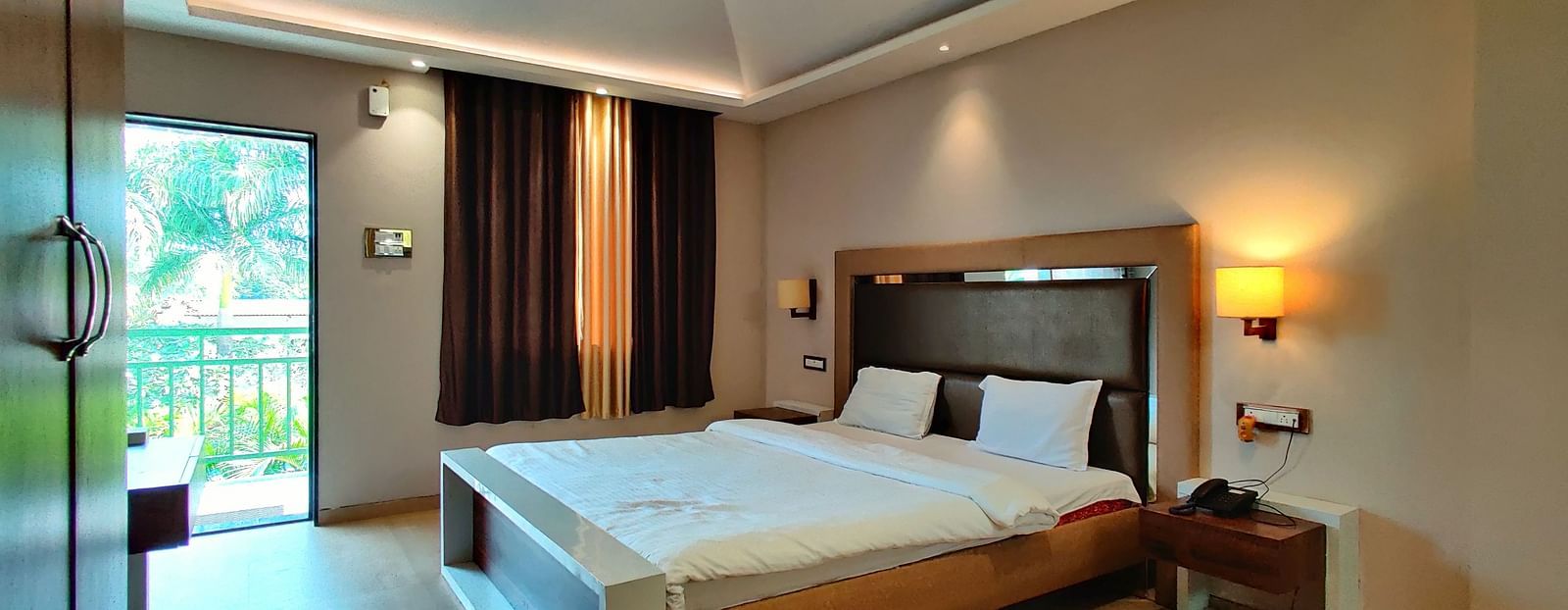 Overview of a Super Premium Room at The Kanila Resort with a queen sized bed, a nightstand, a TV, and a desk. 