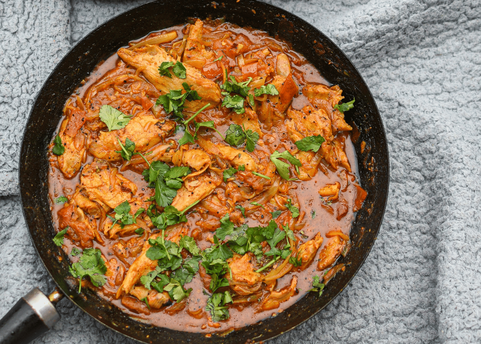 Chicken curry cooked in a pan with rich gravy and garnished with fresh coriander leaves.