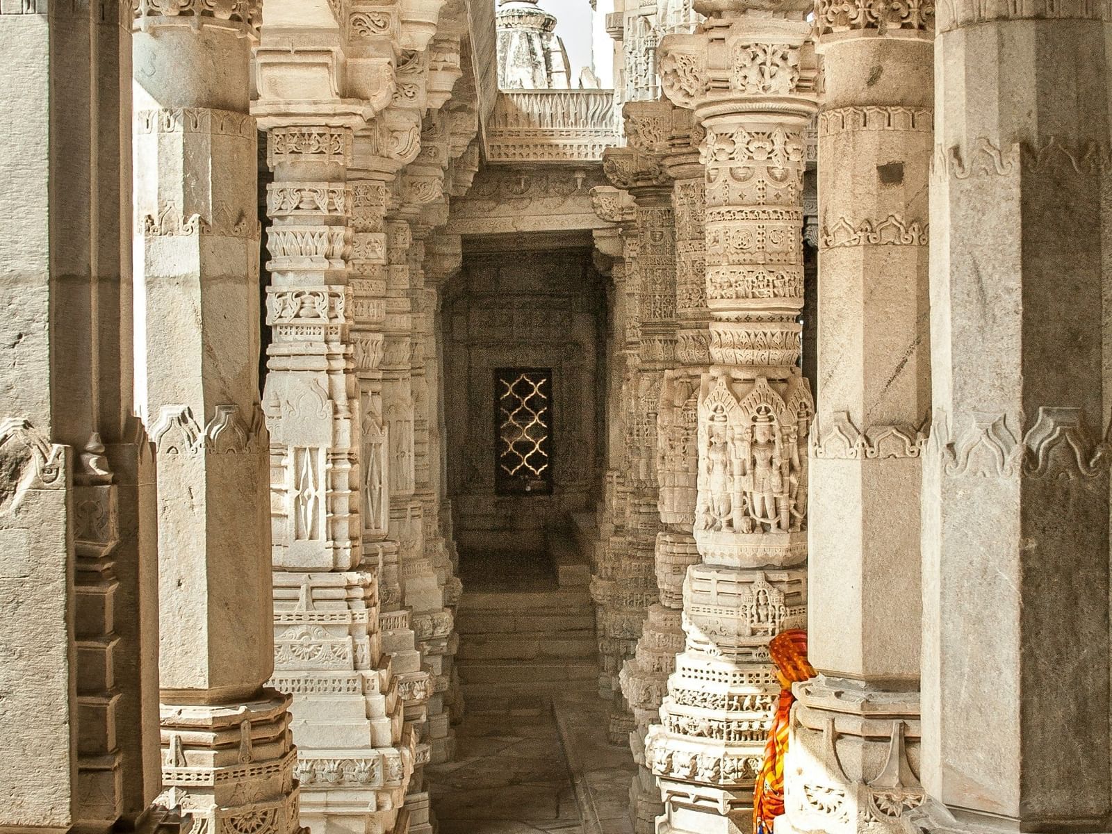  A hallway in a temple with a long corridor of intricately carved marble pillars, leading to an ornate window at the end.