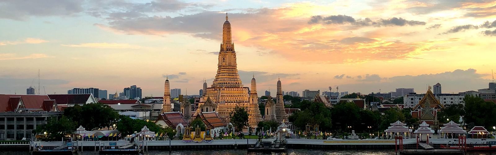 a temple in gold colour situated in front of the river front with buildings text to it