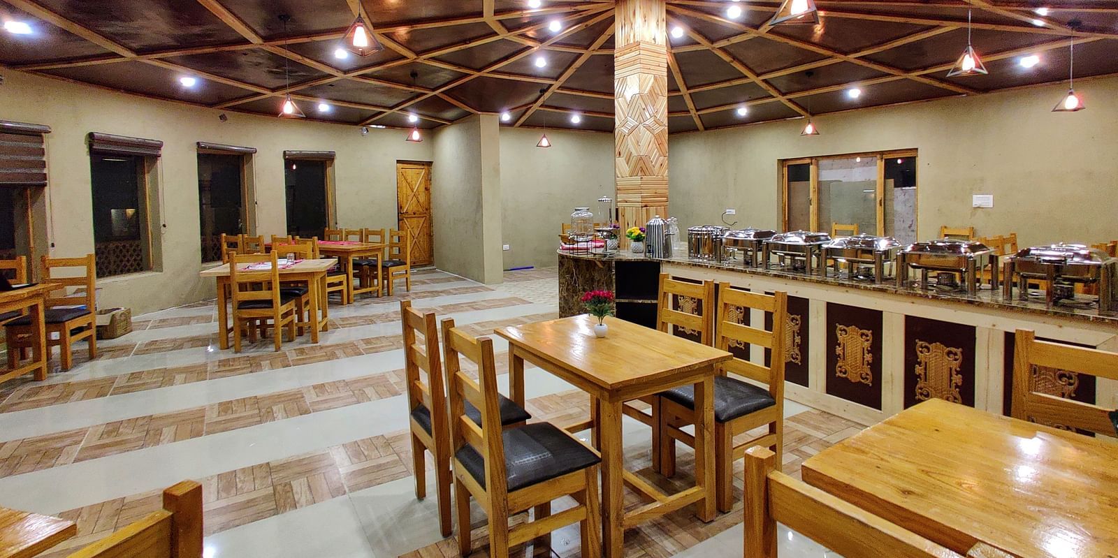 The interior of a dining area at White Sands Resort, Ladakh highlighting the wooden furniture, ceiling design, and buffet area.