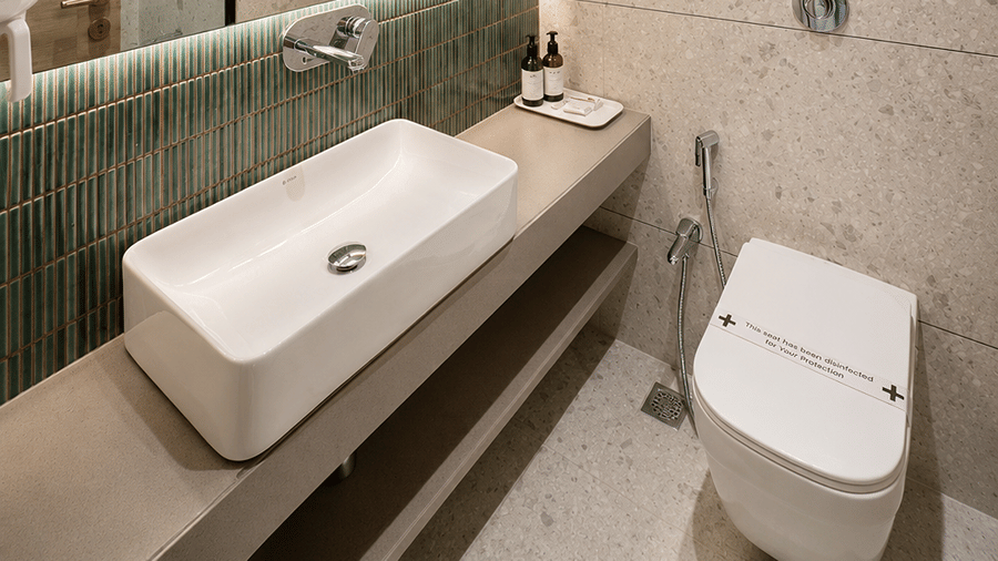A bathroom with a sink, a toilet seat, a mirror, and other toileteries. | The Oriental Residency