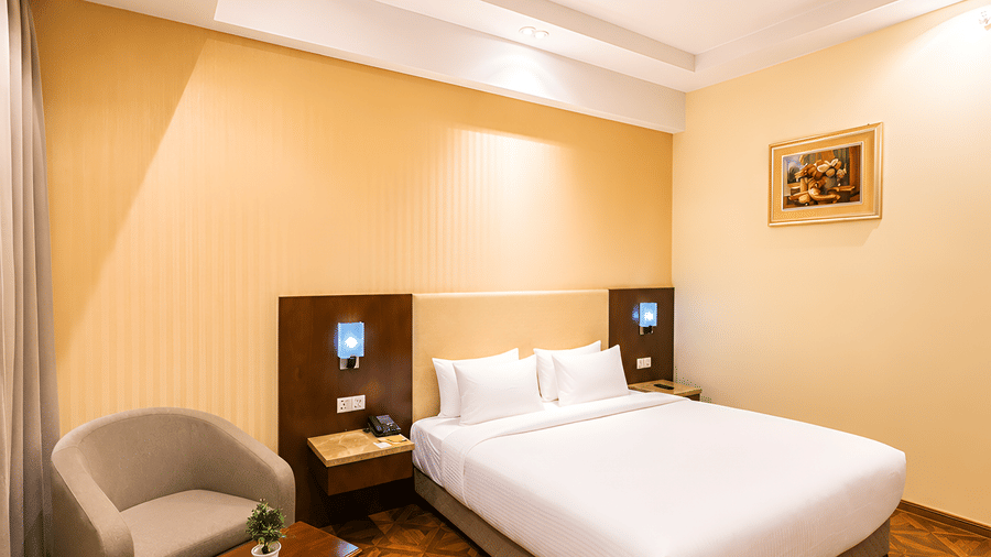 Compact view of the Deluxe room at Golden Tulip Kukas Jaipur with a king bed, armchair in the corner, patterned carpet, and warm ceiling lighting