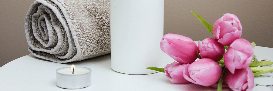 Pink tulip flowers kept on a white table along with towel and scented candle