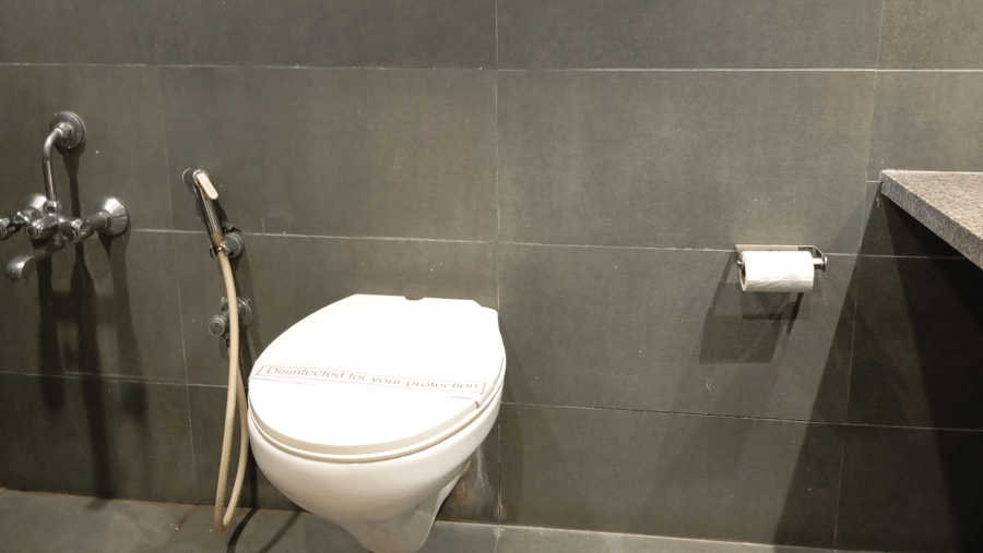 A contemporary bathroom at Hotel Ashray Inn Express with a mounted toilet, handheld shower, flush panel, and tiled interiors.