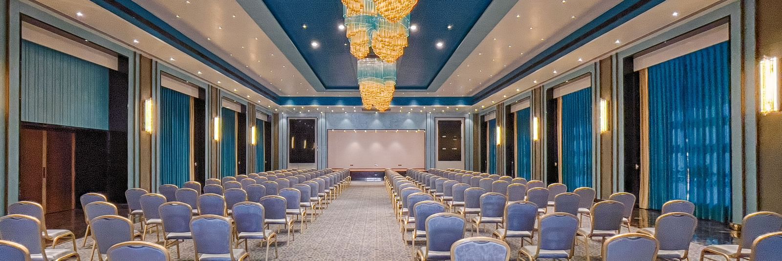 An elegant banquet with colourful and well designed interiors with long, fancy chandeliers - Crescent Resorts