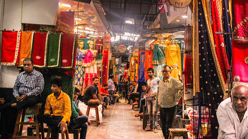 A long view of Sindhi Market, bustling with sellers offering a variety of clothes and goods, while people sit and relax near the vibrant shops.