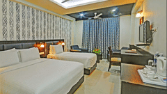 Modern hotel room with king bed and a single bed, grey curtains, wooden furniture, and seating area at Pride Ananya Resort Puri