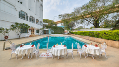 Tables and chairs placed next to the swimming pool with crystal blue water at The Pride Premier Nagpur