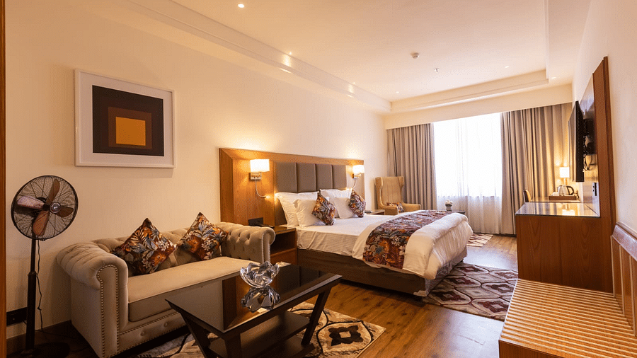 Luxurious hotel room with a king size bed, tufted sofa, glass coffee table, armchair, and a wall-mounted TV - Clarks Inn Express, Ludhiana