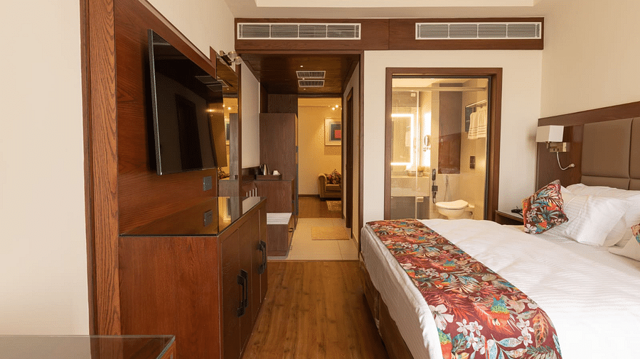 Elegant hotel suite featuring a cosy king-size bed, wooden furnishings, a wall-mounted TV, and a well-lit bathroom with a glass partition - Clarks Inn Express, Ludhiana