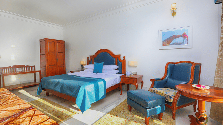 Spacious deluxe room featuring double bed, wooden furniture, work desk, and warm lighting at Fateh Niwas, Udaipur.