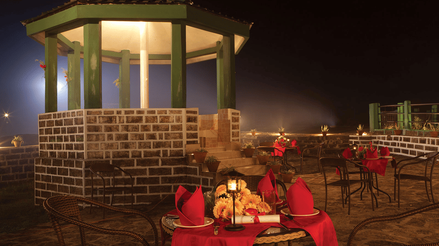 Outdoor candlelit dinner gazebo at Polo Resort Cherrapunji with red linens, sunflower centrepiece, lantern, brick base and night mist.