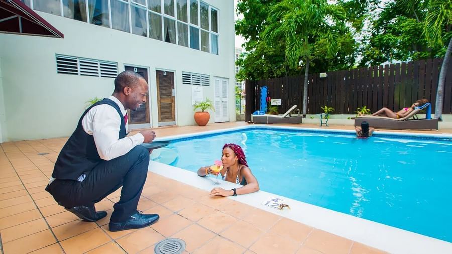 A person in a uniform handing a drink to a lady in a swimming pool | Altamont Court, Jamaica