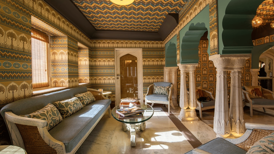 A room at Surya Haveli, Amer Fort Jaipur, with ornate wall patterns, carved arches, classic seating, and a central coffee table in an elegant palace-inspired setting.