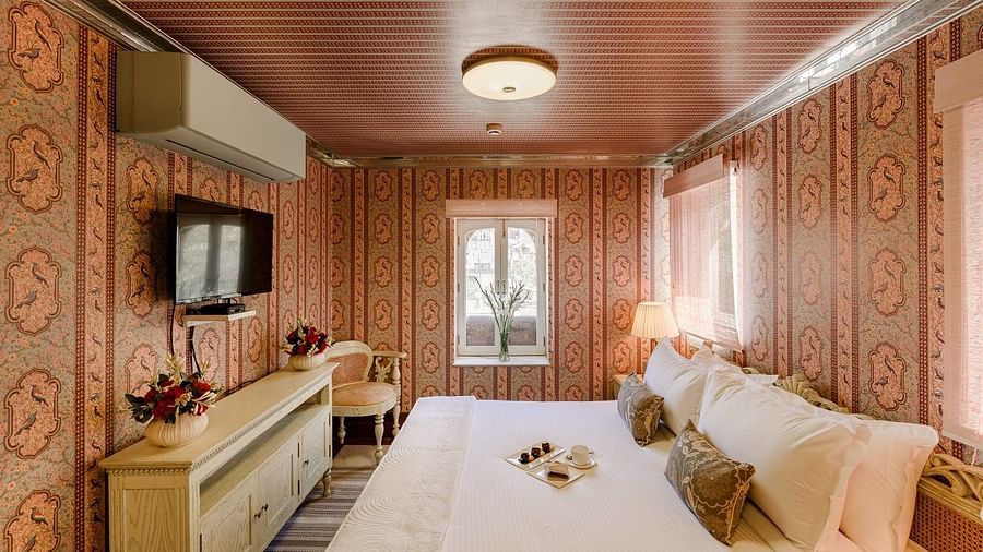 Fancy room at Surya Vilas in Jaipur featuring walls decorated with traditional artwork and a plush bed facing the TV mounted on the wall