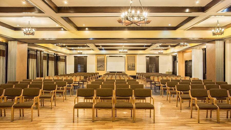 An image of a conference hall with a set of table and chairs in each corner and a projector screen at the front of the room - The Riverview Retreat, Corbett