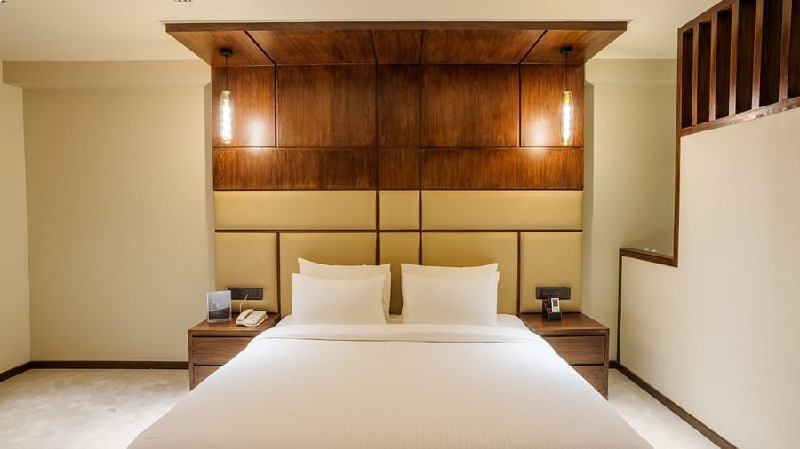 A image of a bedroom from the front with a comfortable bed, warm yellow lighting and a night stand placed to its side 