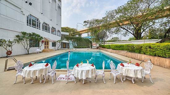 Tables and chairs placed next to the swimming pool with crystal blue water at The Pride Hotel Nagpur
