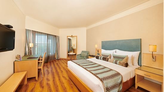 Image of a room at Pride Hotel Nagpur featuring a plush bed with cushioned wooden headboard with wooden nightstands on both sides facing the TV mounted on the wall