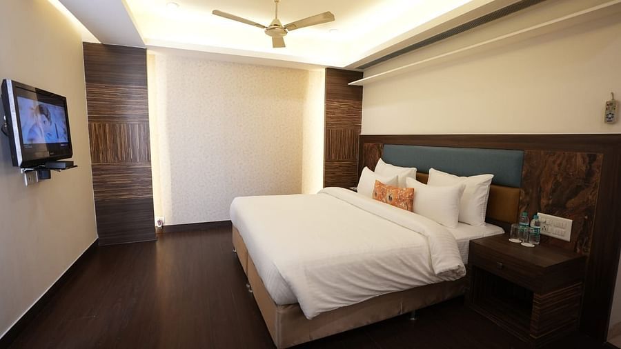A bedroom with a white bed, dark wooden floor, and a mounted television on the wall - VITS Gurugram