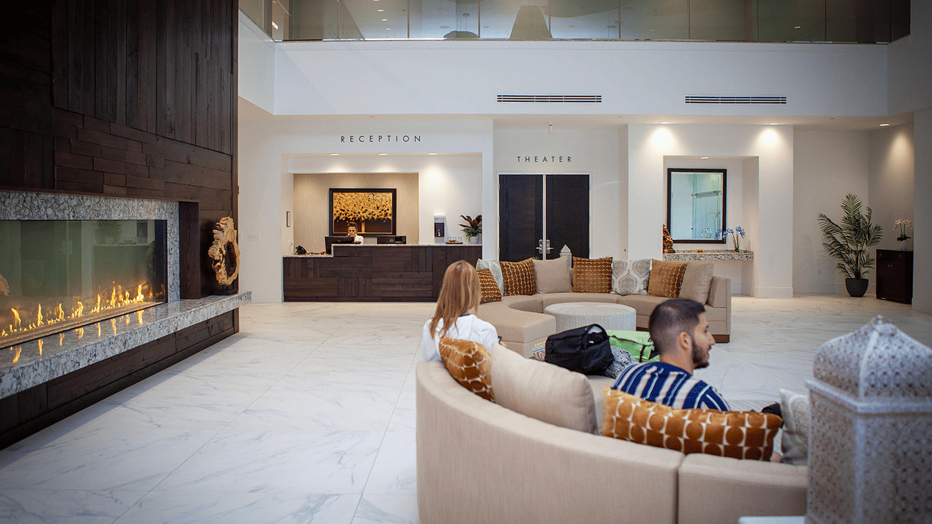 The lobby of YO1 Longevity and Health Resorts with guests seated on a curved sofa near a sleek fireplace, creating a warm and welcoming first impression