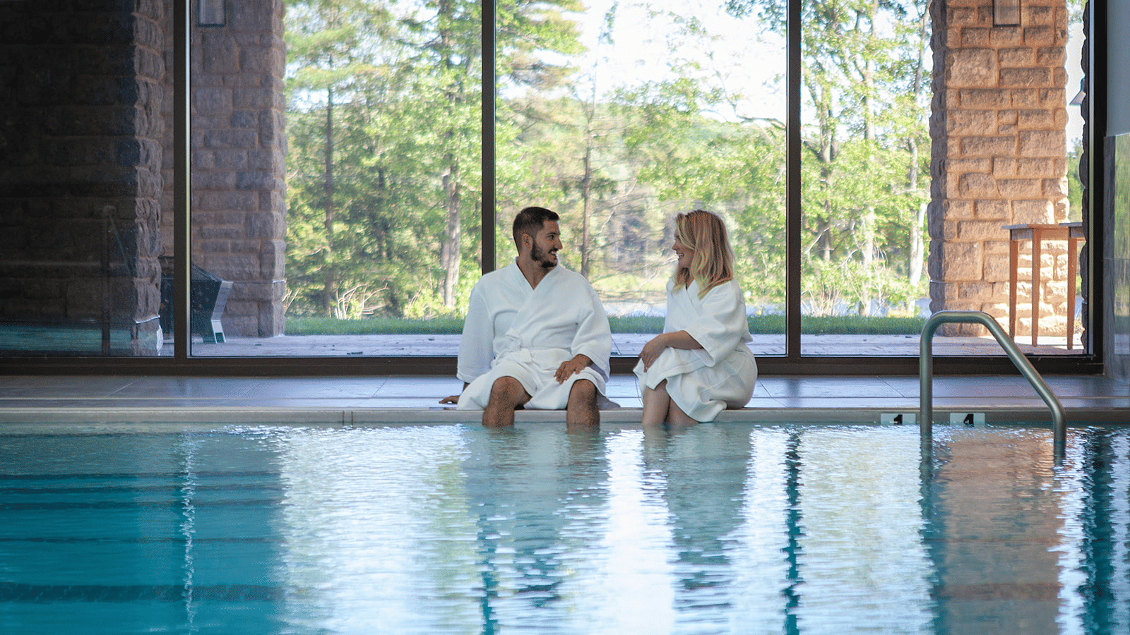 2 individuals in bathrobes interacting with each other at the pool deck with their legs dipped in the water at YO1 Resorts