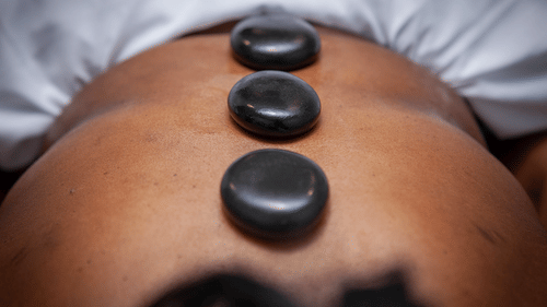 A person lies face down with three smooth, dark massage stones placed in a line down their spine at YO1 Longevity & health Resorts.