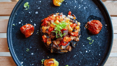 Cooked portobello mushroom stuffed with diced vegetables and topped with fresh herbs placed on a circular plate at YO1 Longevity & Health Resorts