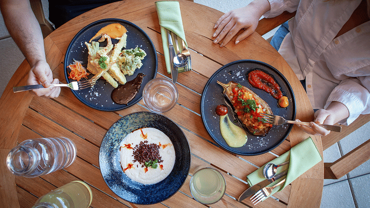 2 people at a wooden table, enjoying three plates of well-plated, gourmet food at YO1 Longevity & Health Resorts, Catskills