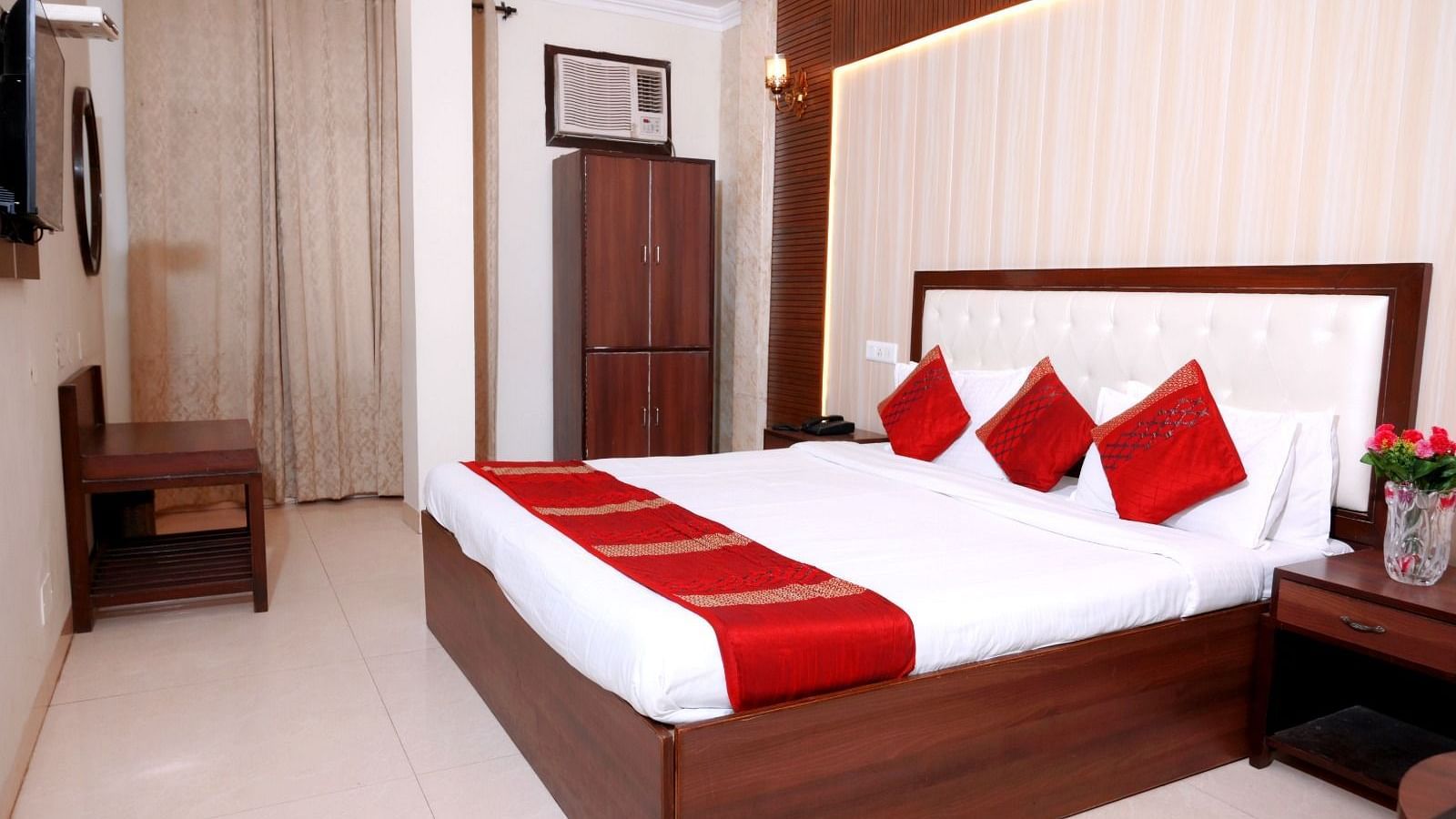 A stylish hotel room with a king-size bed, red and white linens, wooden furnishings, and elegant lighting - Hotel Diamond Inn, Chandigarh