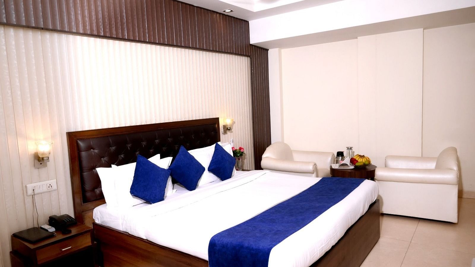 A spacious hotel room with a king-size bed, blue and white bedding, plush headboard, and elegant lighting - Hotel Diamond Inn, Chandigarh