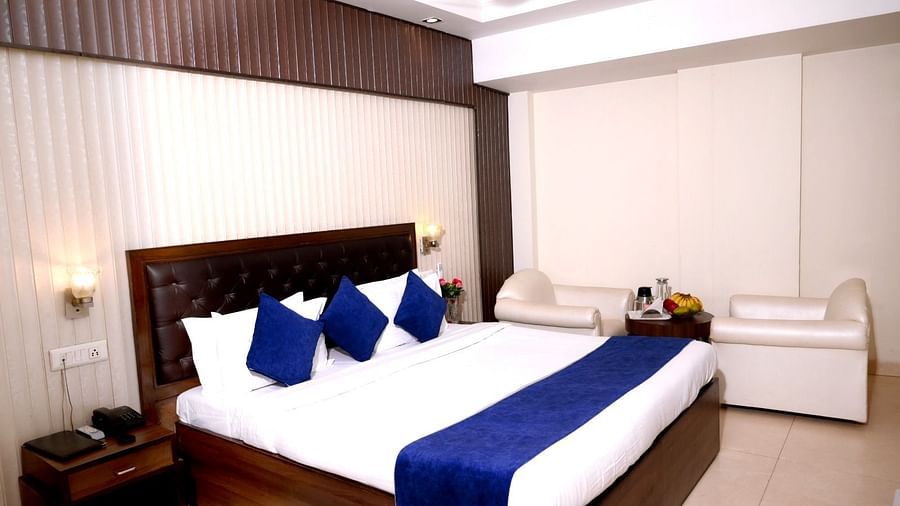 A spacious hotel room with a king-size bed, blue and white bedding, plush headboard, and elegant lighting - Hotel Diamond Inn, Chandigarh