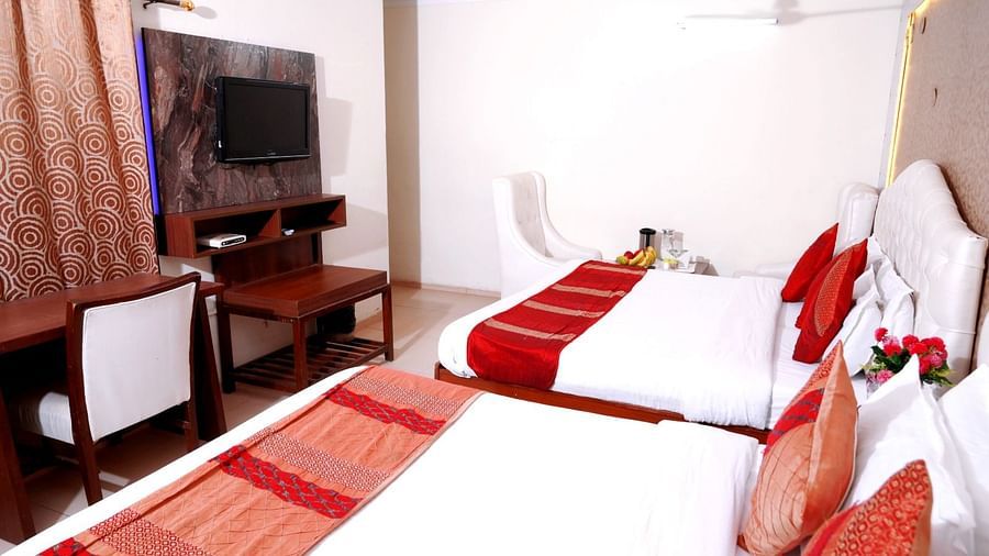 A well-lit hotel room with a king-size bed, red and white bedding, a flat-screen TV, and a cosy seating area - Hotel Diamond Inn, Chandigarh