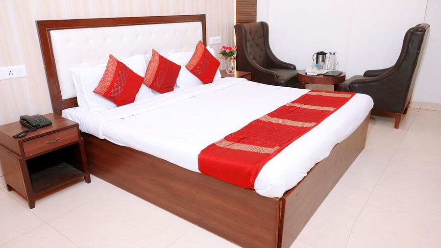A stylish hotel room featuring a king-size bed with red and white linens, dark wooden furnishings, and a comfortable seating area - Hotel Diamond Inn, Chandigarh